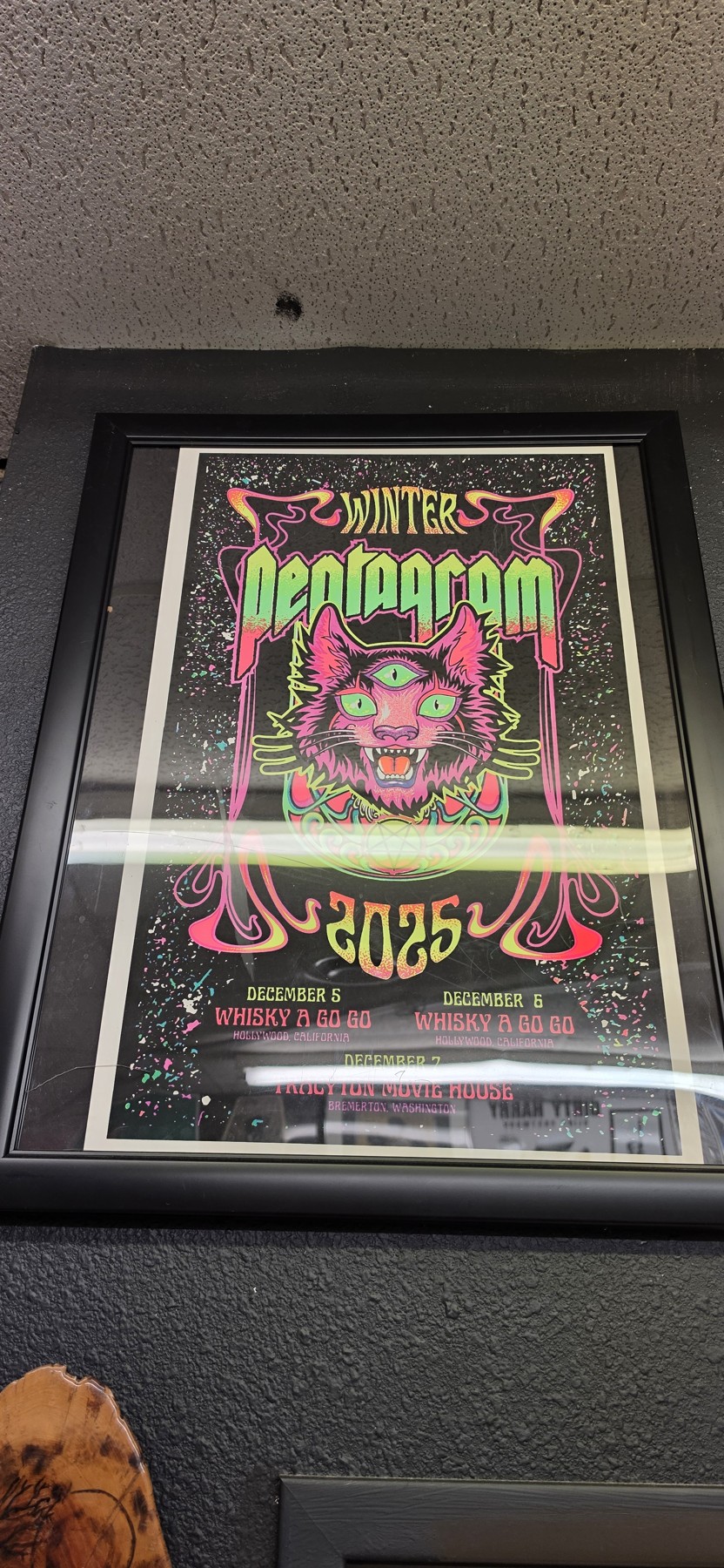 Framed neon green and pink Pentagram Winter 2025 poster on a black wall